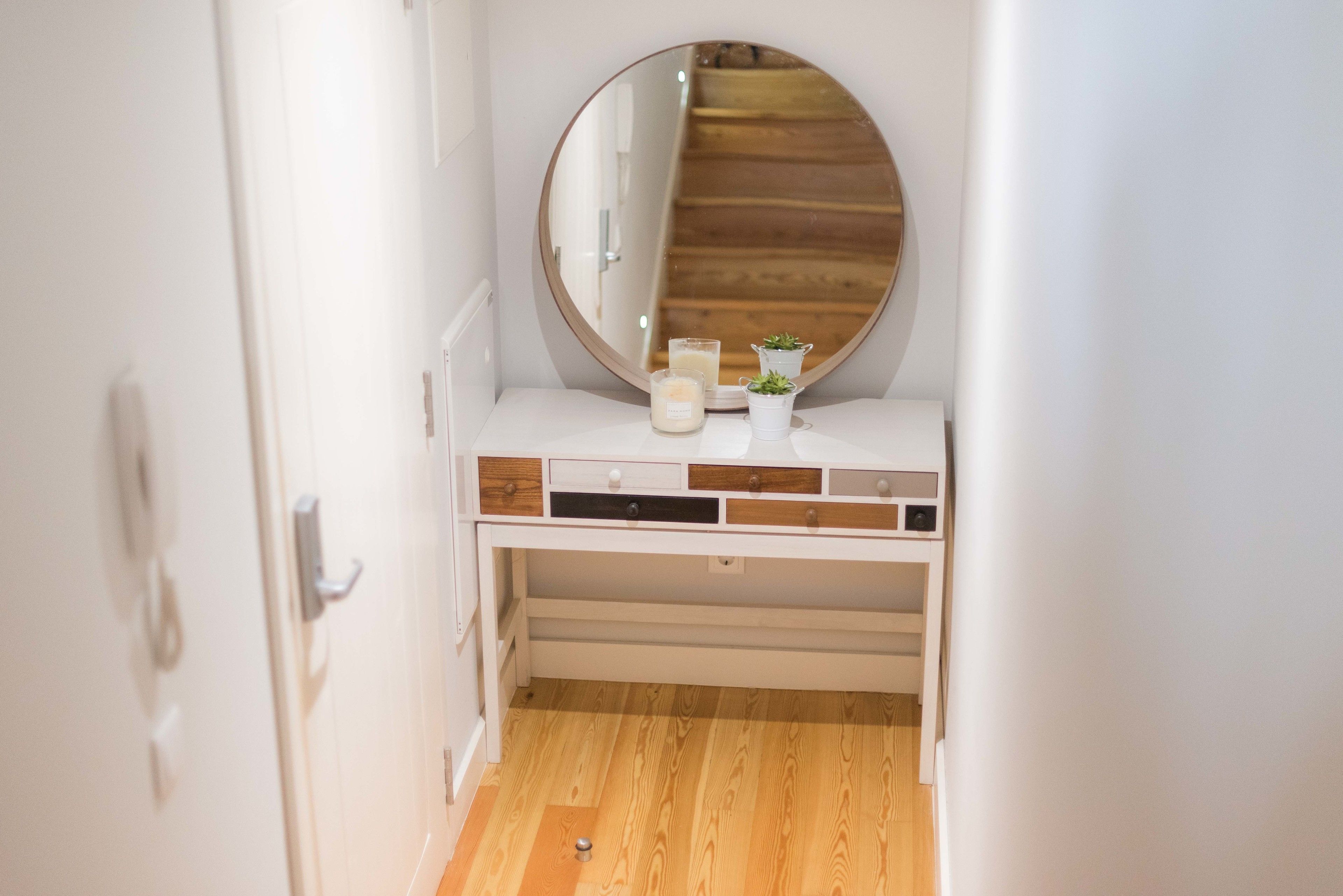 A narrow hallway with a white vanity featuring a round mirror, a small potted plant, and candles.