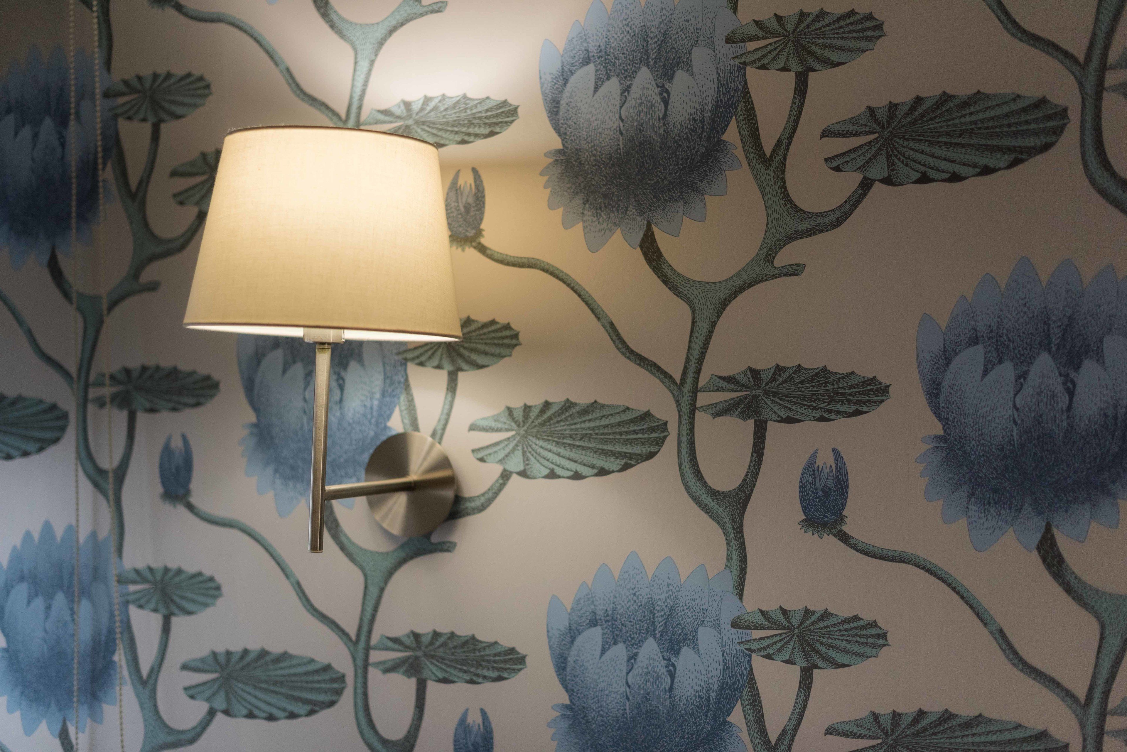 Un mur recouvert d’un papier peint à motifs floraux et une lampe fixée au mur.