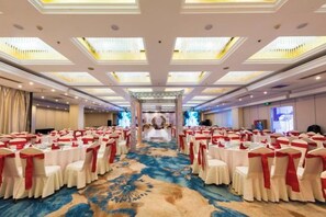 Une salle de banquet avec des tables rondes disposées en rangées, une allée centrale et un sol recouvert de moquette.