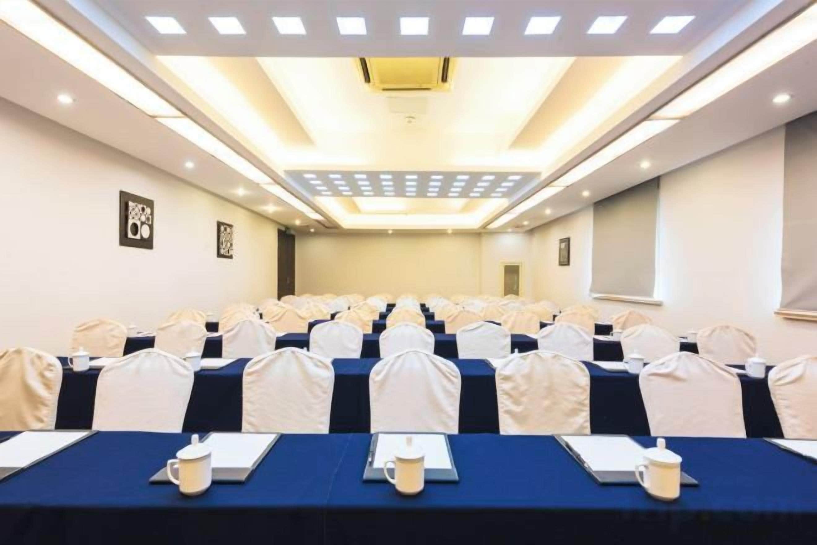 A conference room with rows of tables, chairs, and a ceiling light fixture.