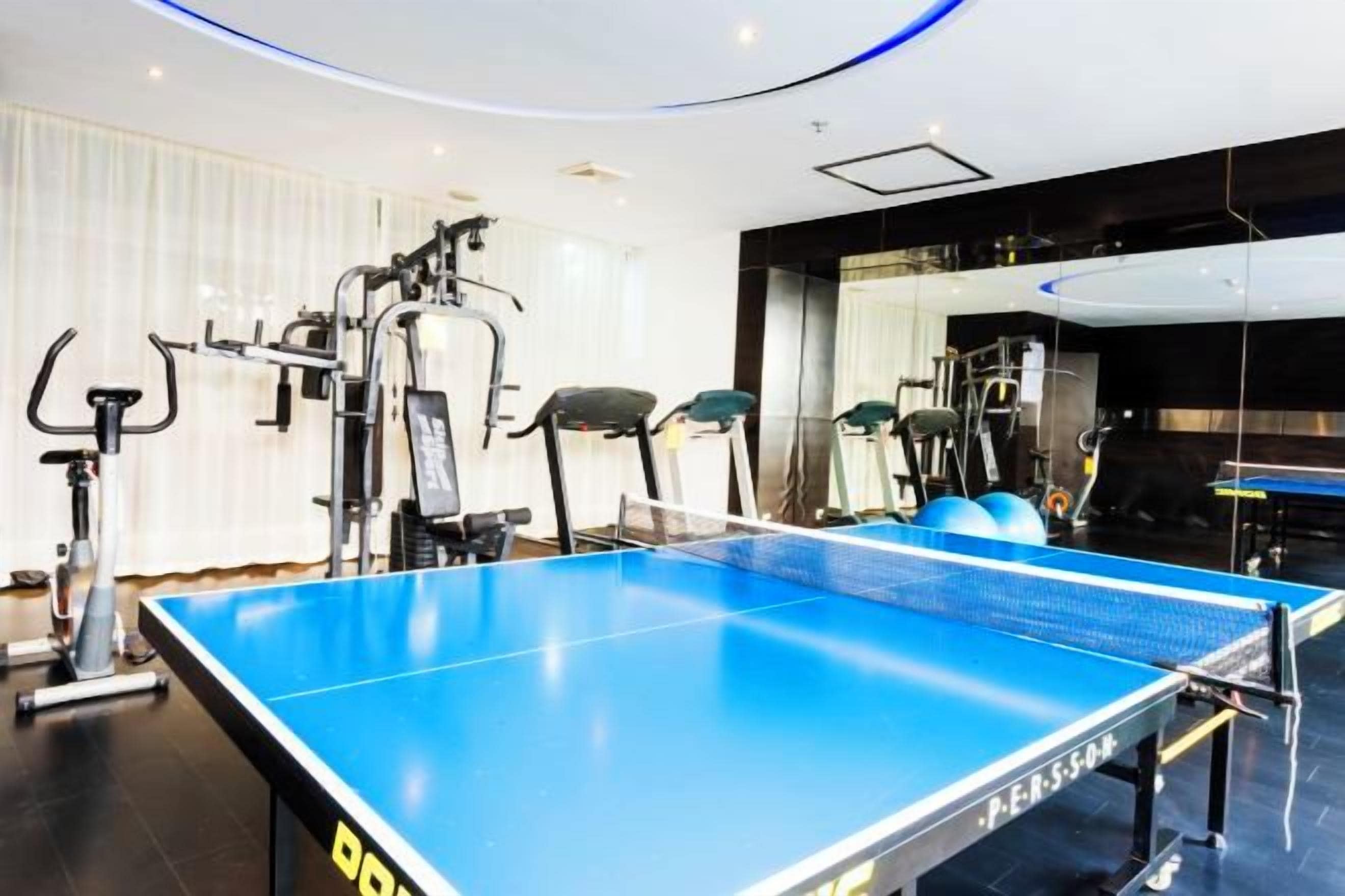 A room with a ping pong table, exercise equipment, and a mirror.