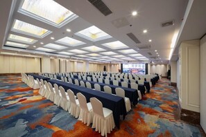 Une salle de conférence avec des rangées de tables et de chaises, de grandes fenêtres et un sol recouvert de moquette.