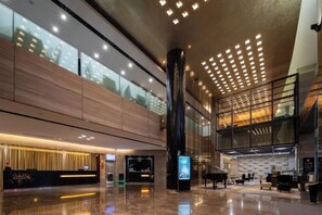 A spacious lobby with a reception desk, a large pillar, and a mezzanine level with seating. - Huaqiao Hotel (Nantong)