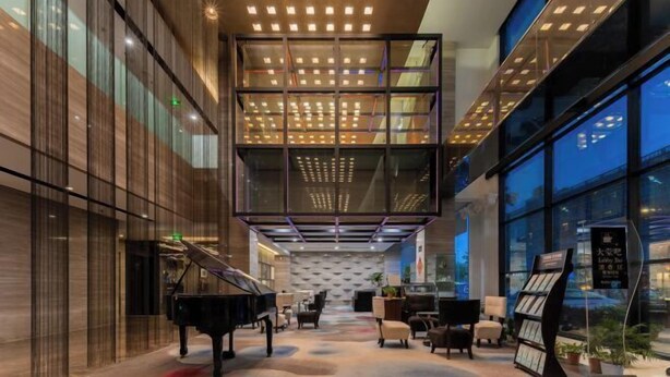 A modern lobby with a grand piano, seating area, and a glass ceiling. - Huaqiao Hotel (Nantong)
