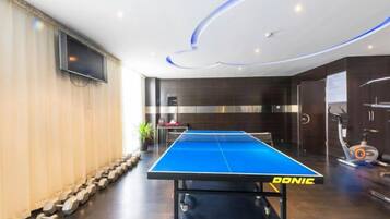 A ping pong table in a modern room with a TV, exercise equipment, and a stone wall.