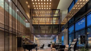 A spacious lobby with a grand piano, seating area, and a large glass wall offering a view.
