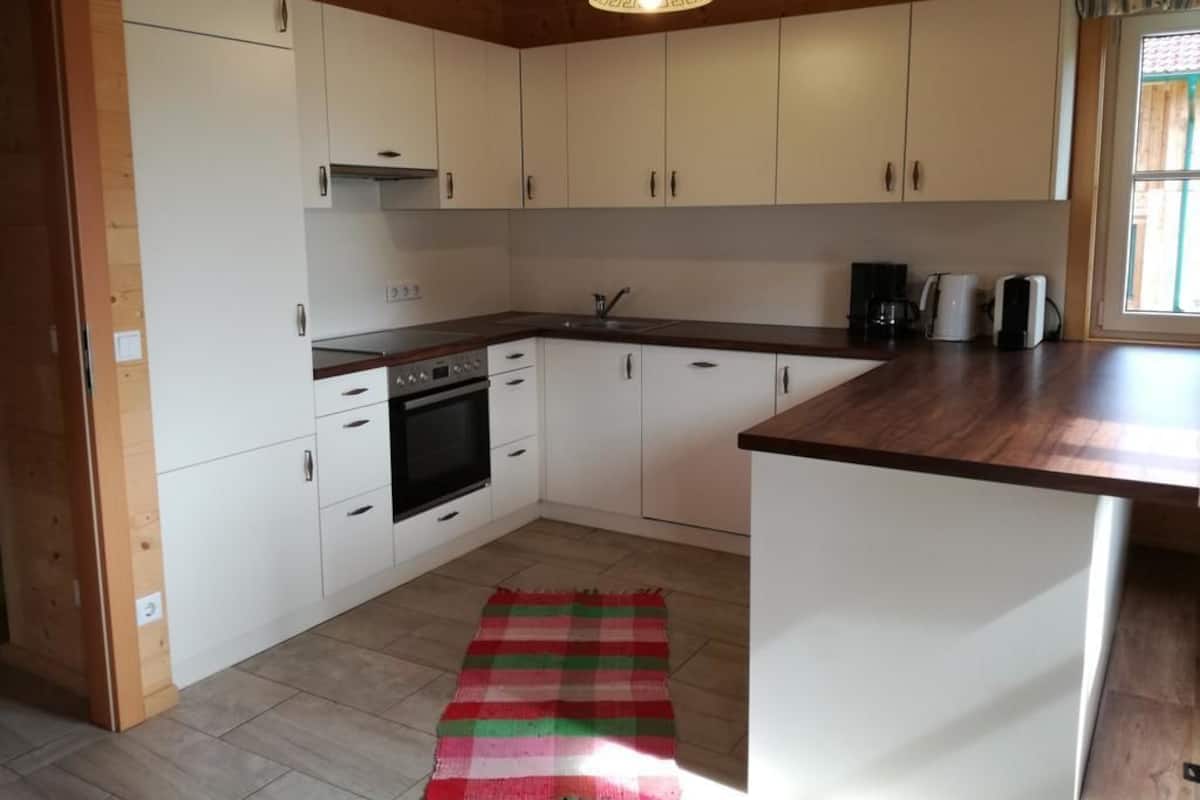 A kitchen with white cabinets, a wooden countertop, a red and green striped rug, and a hanging light fixture.