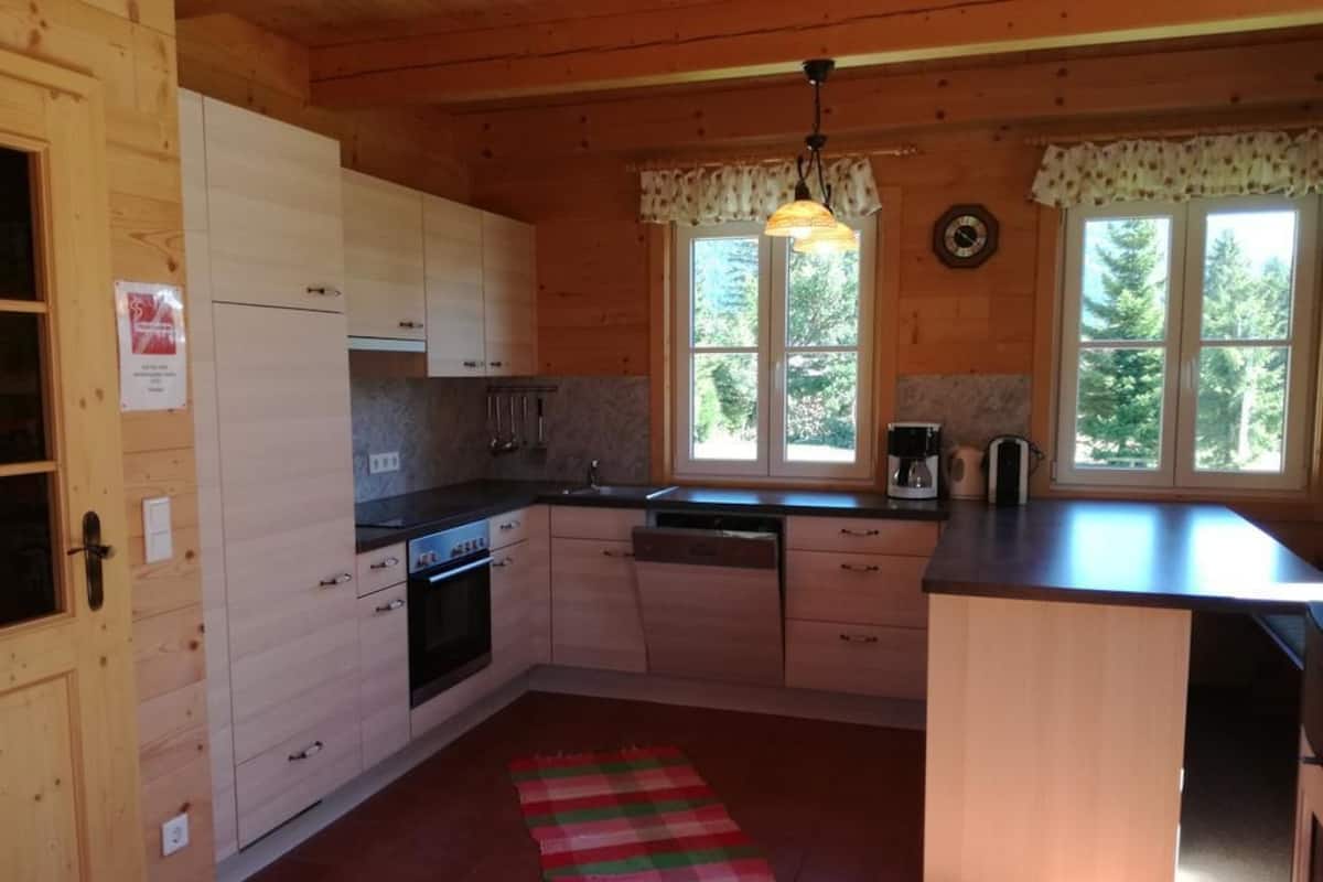 A compact kitchen with wooden cabinets, a built-in oven, a sink, and a window with a view of trees.