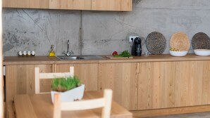 A modern kitchen with wooden cabinets, a sink, and a dining area with a table and chairs. - Casa Do Mercado (Funchal)