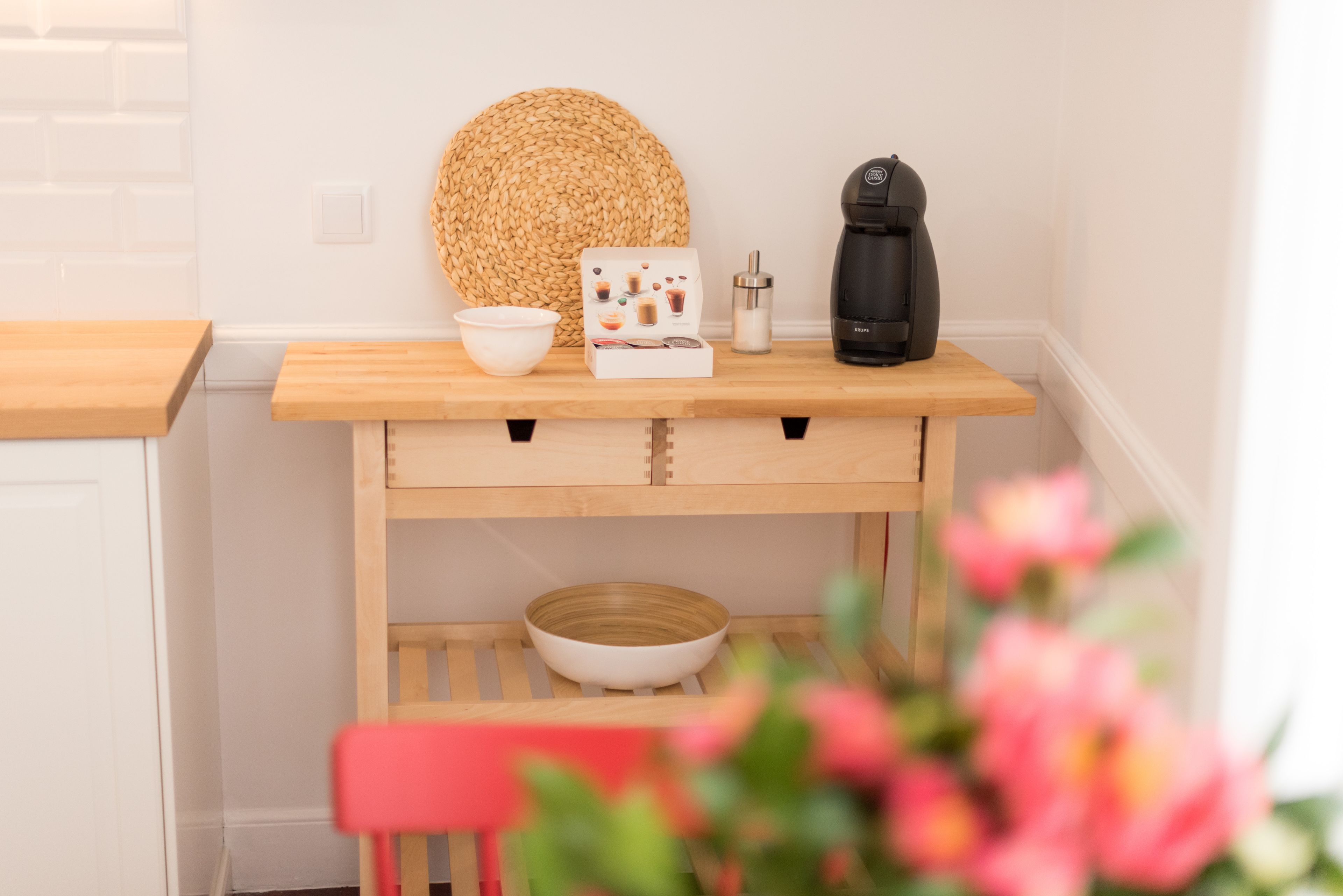 A kitchen area with a wooden table, a coffee maker, a bowl, and a woven basket.