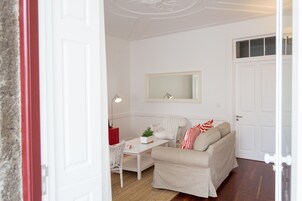 Ein Zimmer mit einem weißen Sofa, einem kleinen Tisch, einem Stuhl, einem Spiegel und einer Tür.