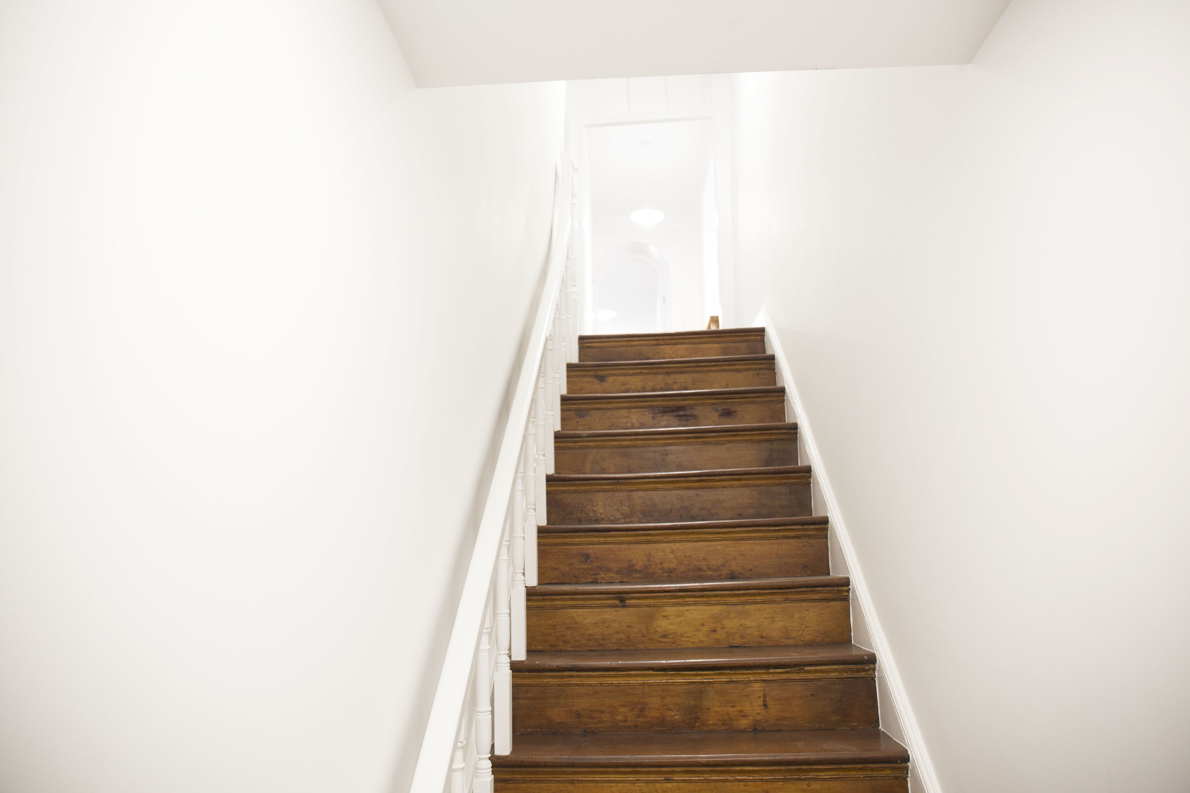 A wooden staircase with white walls and a door at the top.