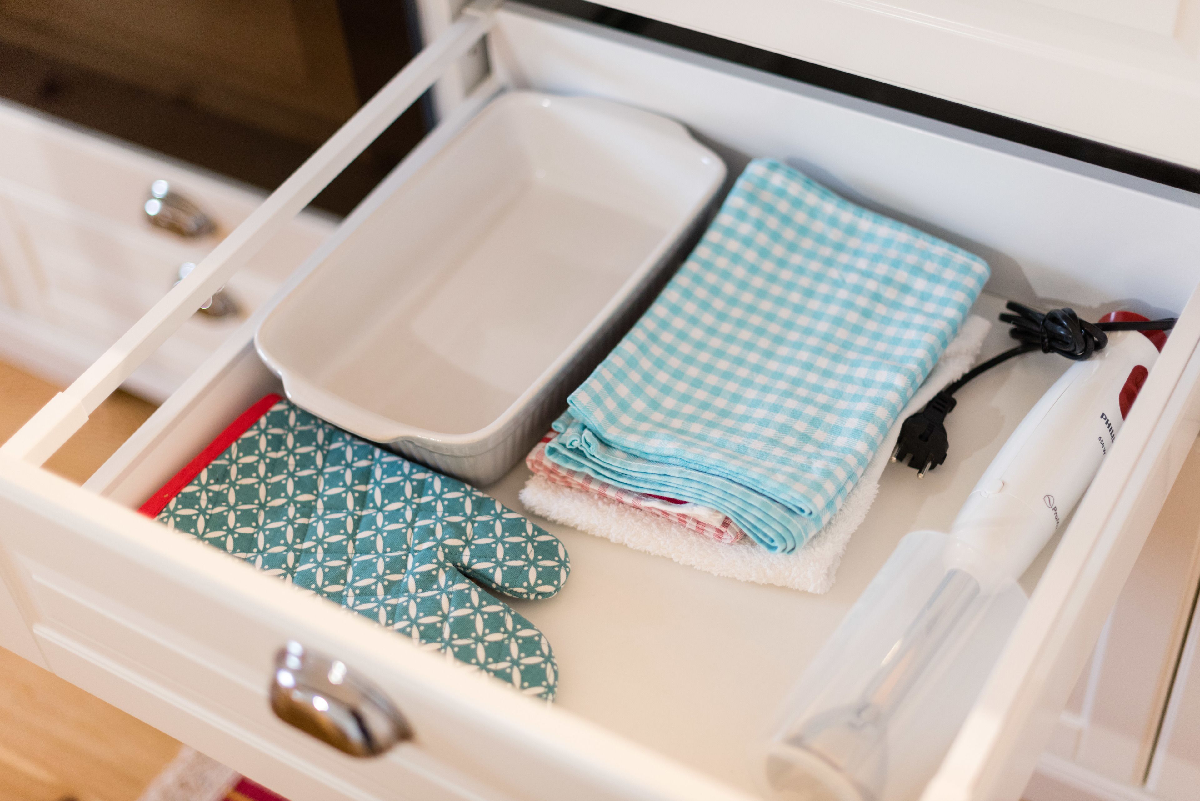 A drawer with a white tray, a folded blue and white checkered towel, a green patterned towel, and a black power cord.