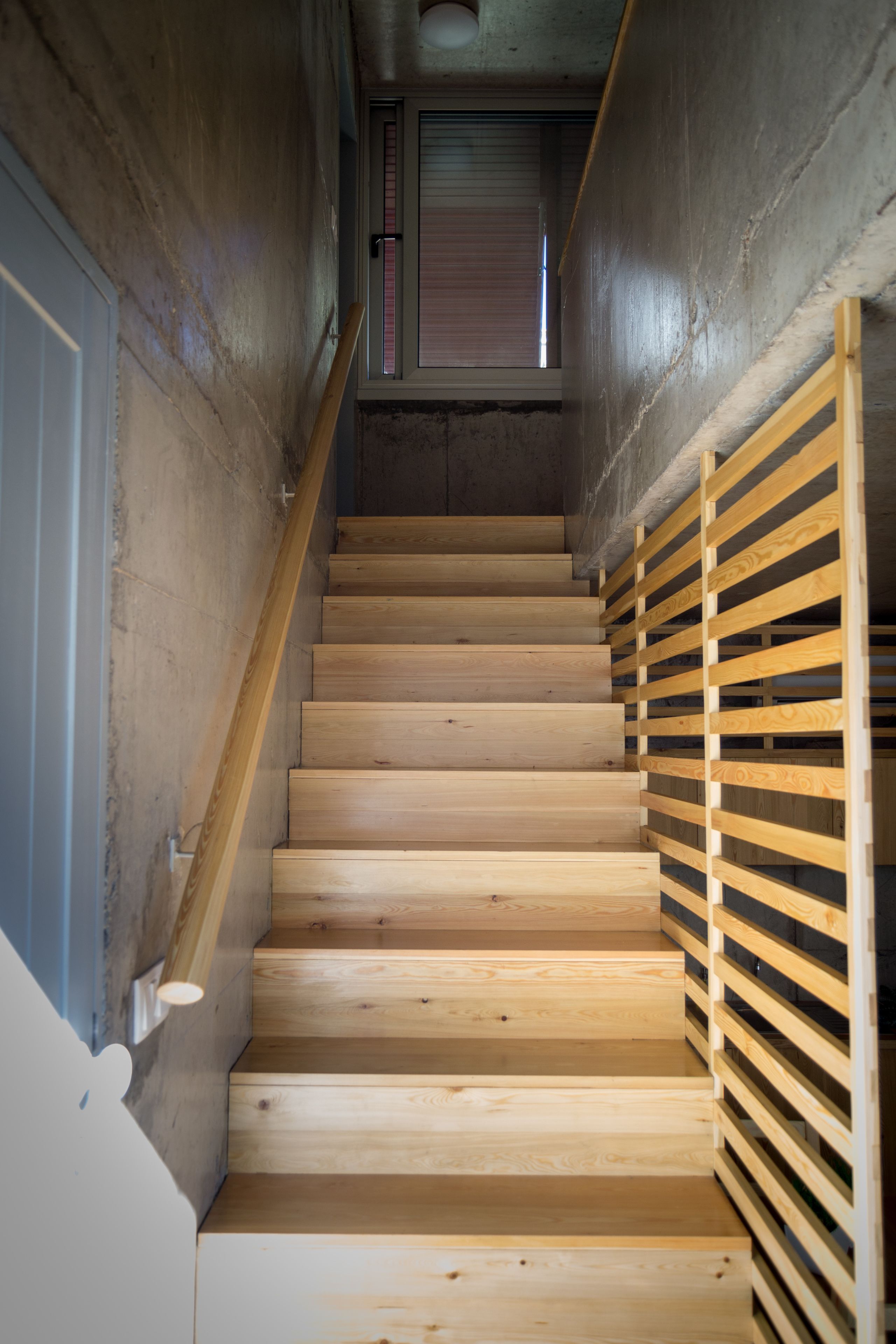 Una escalera de madera con barandilla de metal que conduce a una habitación con ventana y puerta.