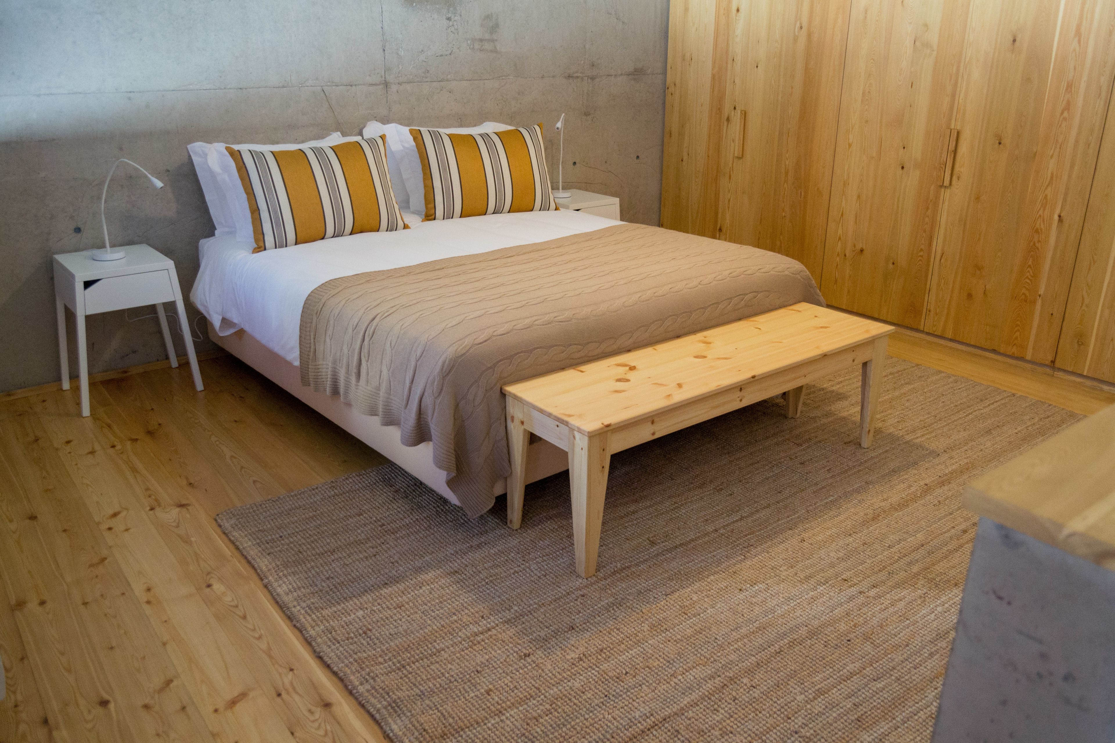 A bedroom with a bed, a wooden bench, a nightstand, and a lamp.