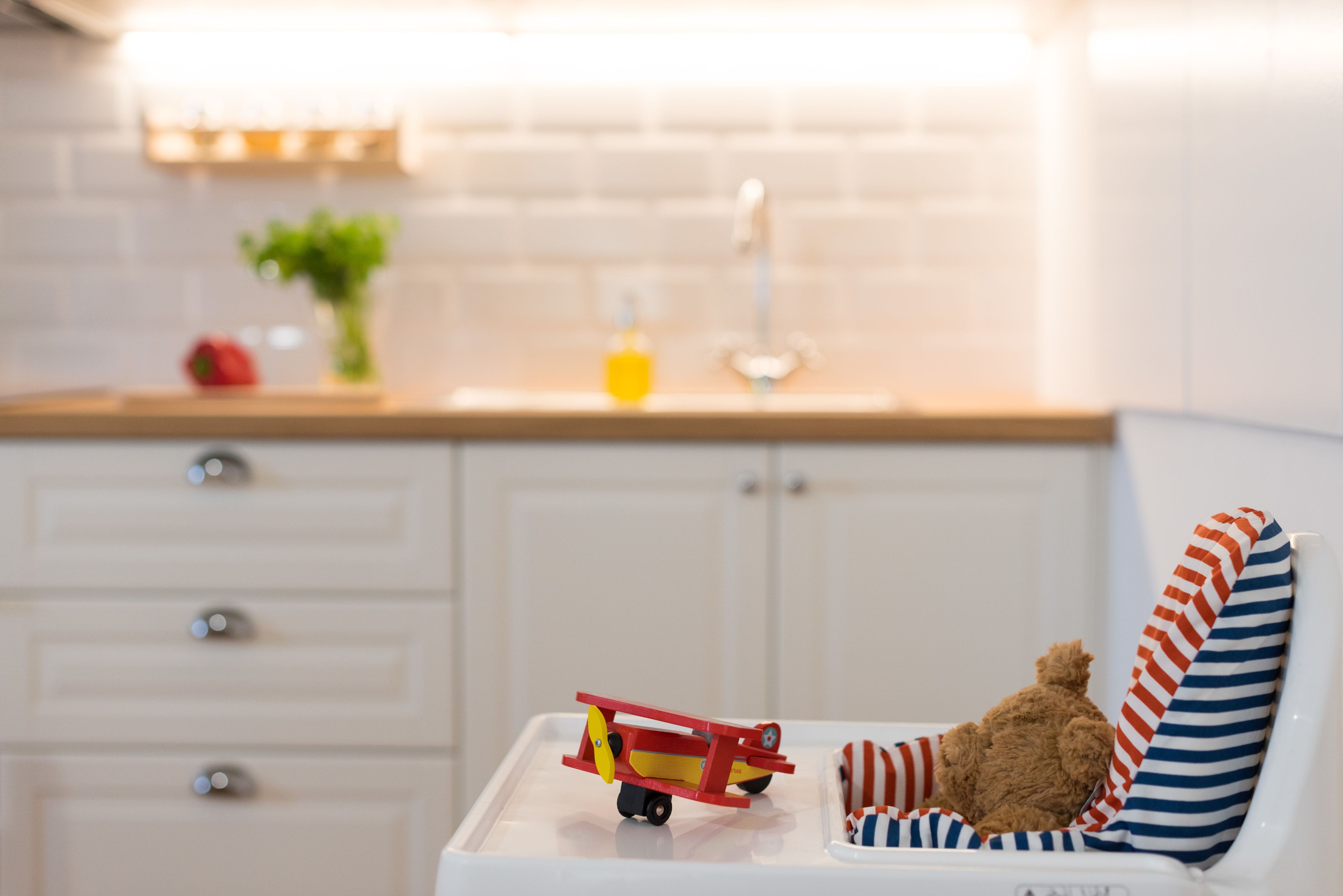 A small, white, child-sized chair with a striped cushion, a teddy bear, and a toy biplane on a white tray.