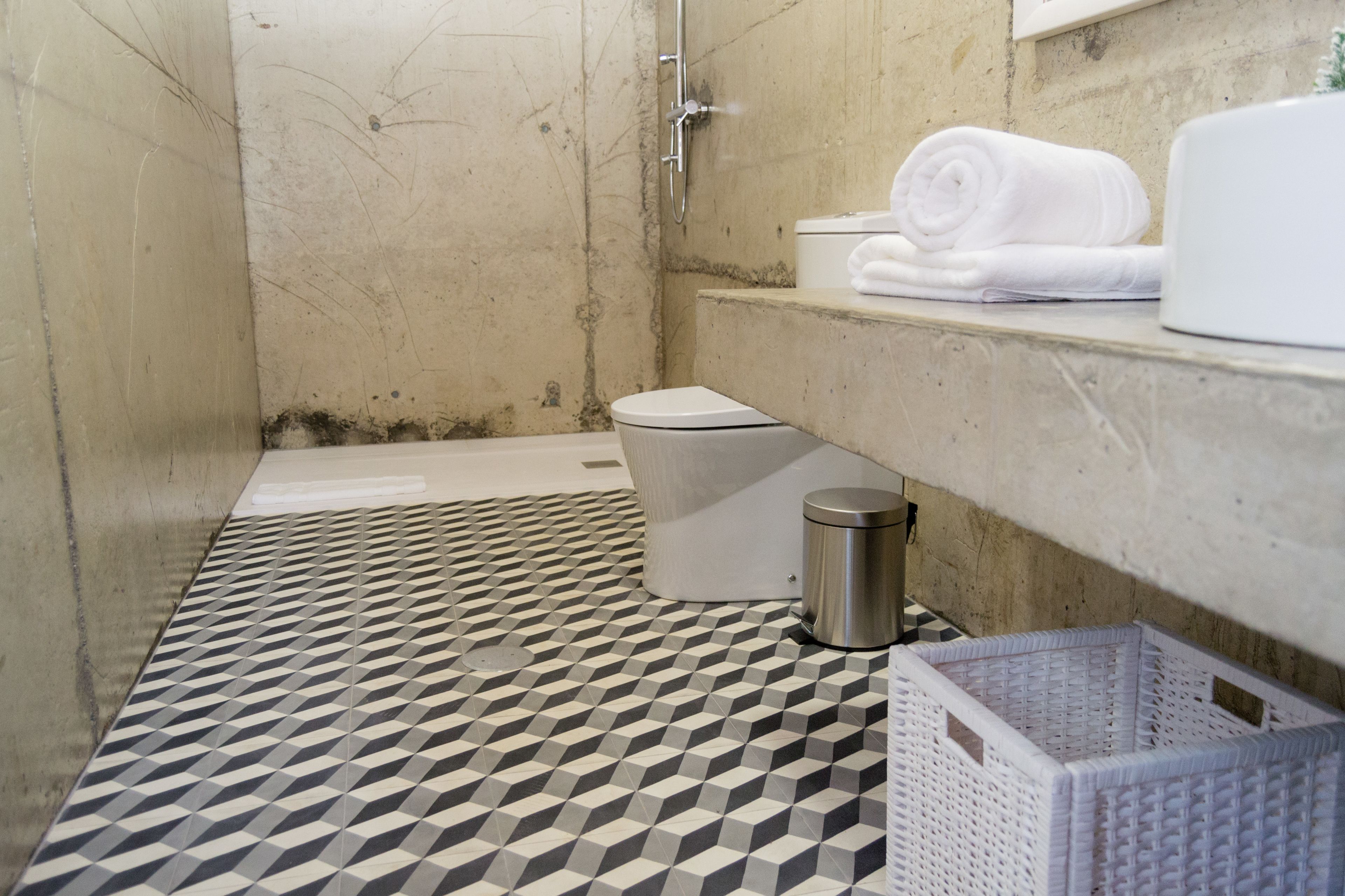 Un bagno con pavimento a motivi geometrici, un water, una vasca da bagno, un cestino metallico e un cesto bianco.