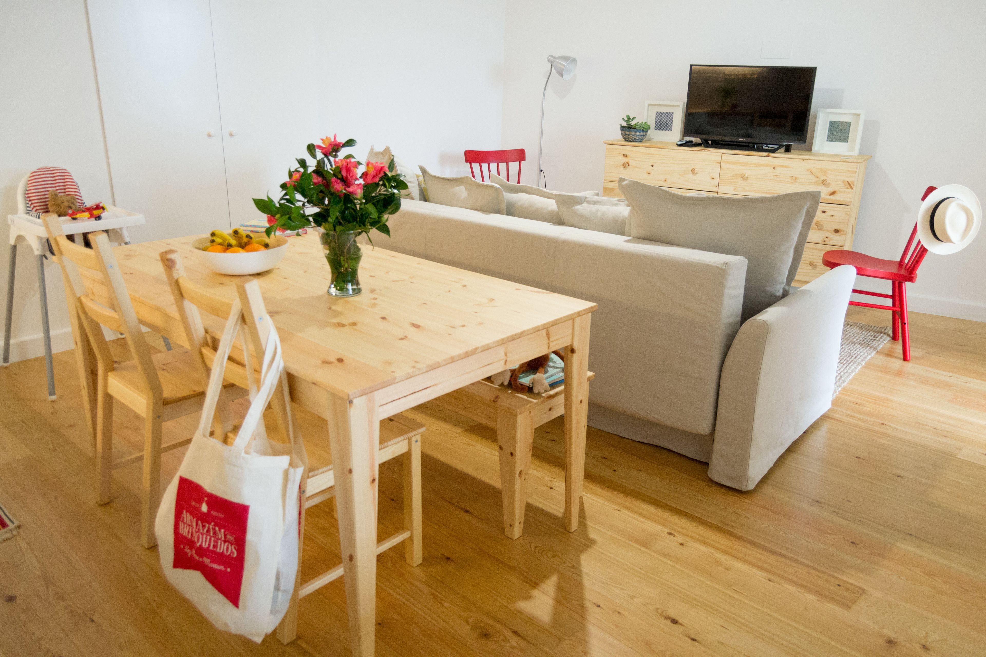 A modern living room with a wooden dining table, a beige sofa, and a TV on a wooden cabinet.