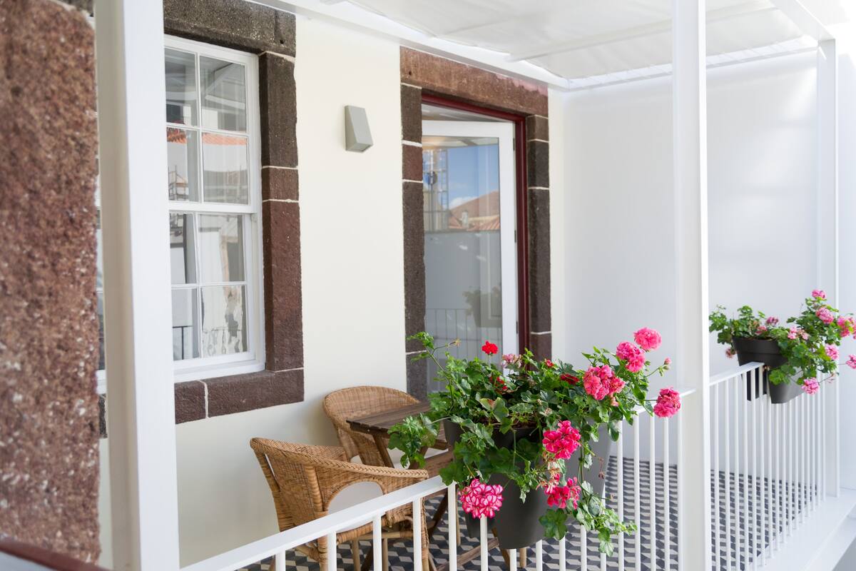 A balcony with wicker chairs, a potted plant with pink flowers, and a white railing.