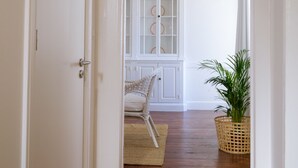 A hallway with wooden flooring, a white door, a wicker basket, and a chair. - Casa Do Mercado (Funchal)