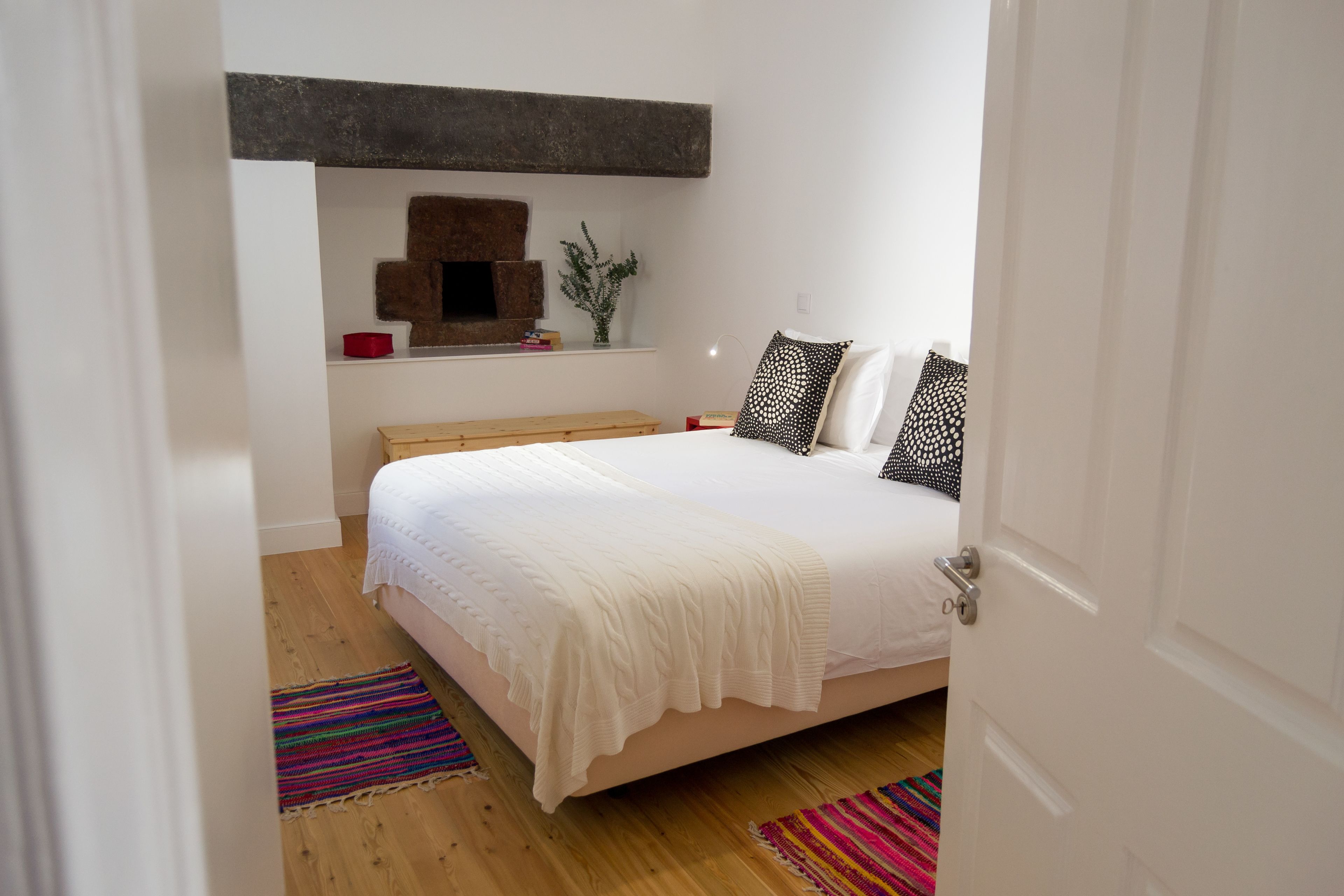 Een slaapkamer met een bed, een bankje, een plank met decoratieve objecten, en een deur.