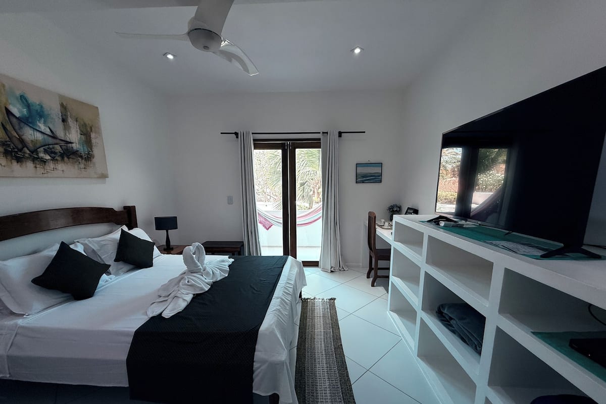 A modern bedroom with a bed, a desk, a TV, and a balcony with curtains.