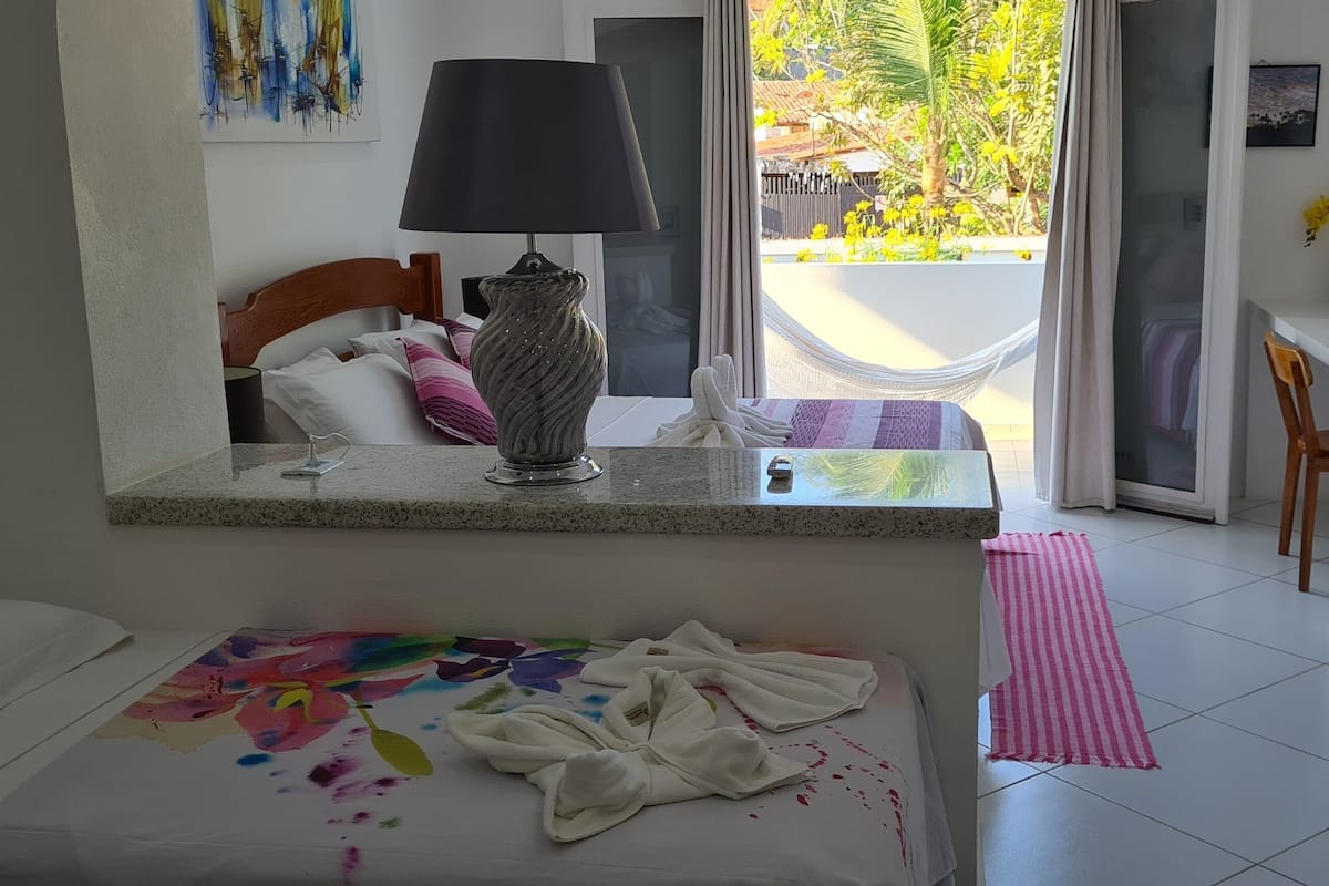 A bedroom with a bed, a bedside table with a lamp, a small desk with a TV, and a view of the outdoors.