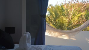 Un lit avec du linge de lit blanc, un rideau bleu et un hamac d’où l’on peut admirer les palmiers.