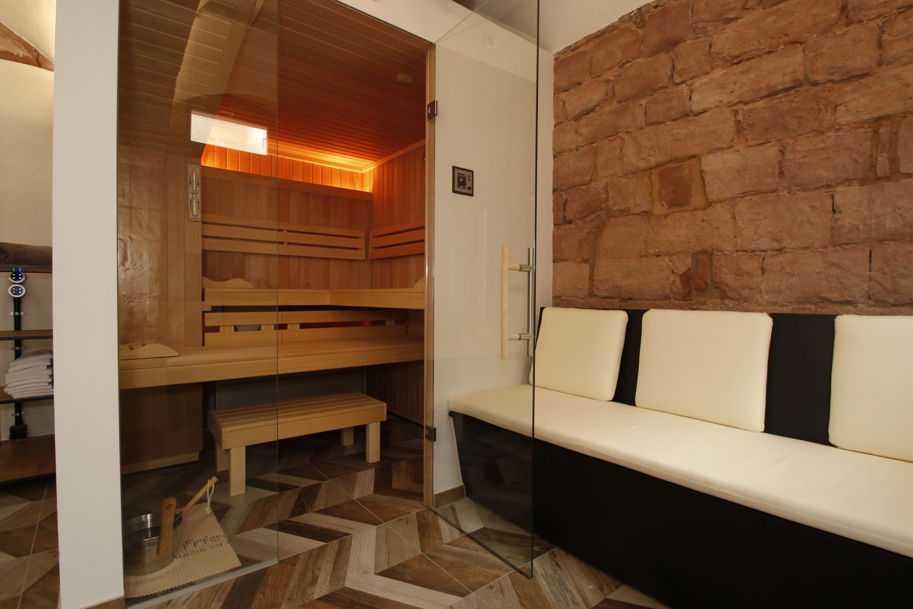 Eine Sauna mit Holzbänken und einer Glastrennwand, einer Bank und einem weißen Sofa mit schwarzen Kissen.