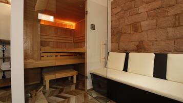 Eine Sauna mit Holzbänken und einer Glastrennwand, einer Bank und einem weißen Sofa mit schwarzen Kissen.