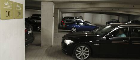 A parking garage with cars parked in designated spaces, concrete pillars, and a tiled floor.