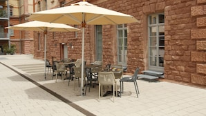 An outdoor café with tables and chairs, set against a stone building with large windows. - Amelie N°1 Hotel & Appartements (Landau in der Pfalz)