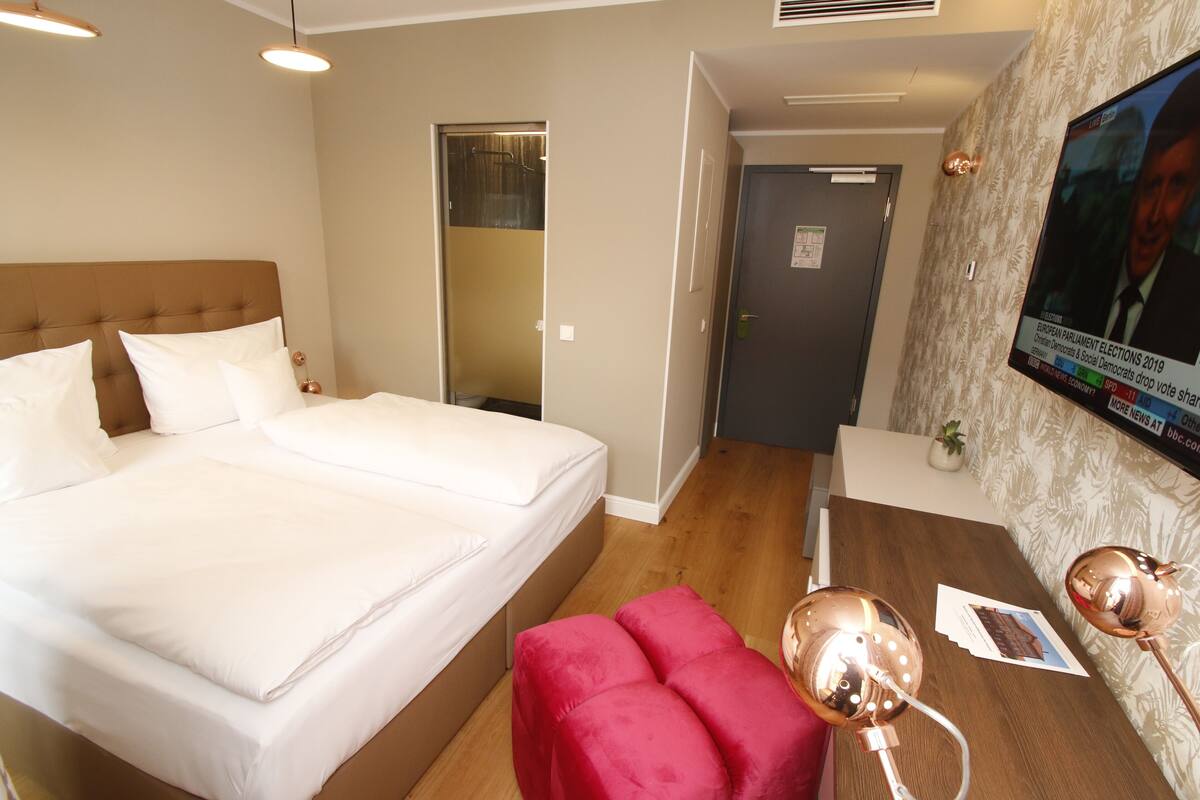 A hotel room with a large bed, a desk with a lamp, and a television on the wall.