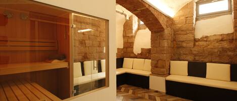 Un cuarto de sauna con bancos de madera, una puerta de cristal, paredes de piedra y un suelo con estampado de espiga.