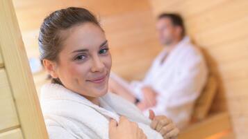 A sauna room with wooden benches and a person in a white robe.