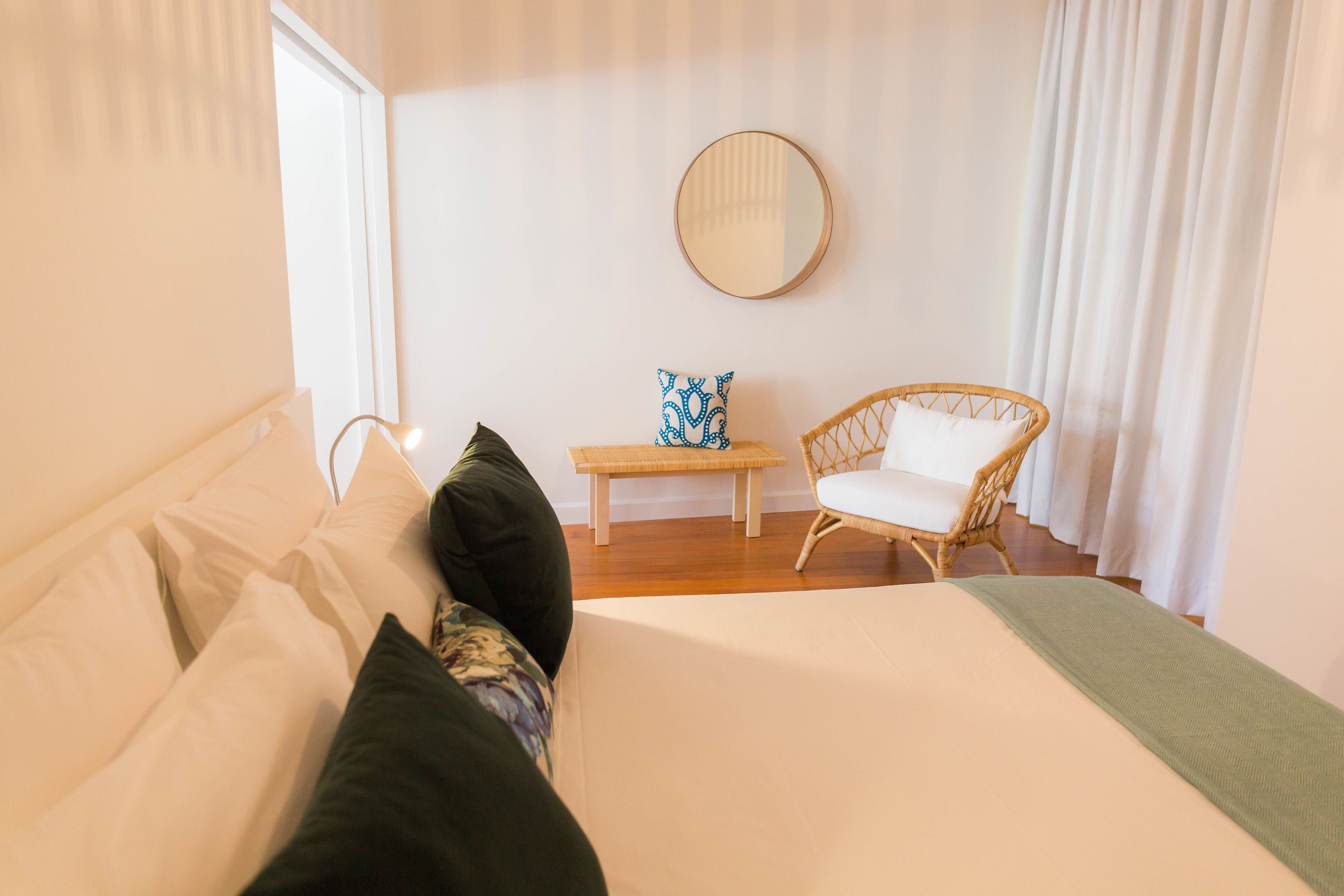 Une chambre à coucher avec un lit, des oreillers, une petite table, une chaise et un miroir au mur.