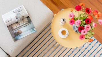 A top-down view of a room with a sofa, a magazine, a coffee table with a cup and saucer, and a vase with flowers.