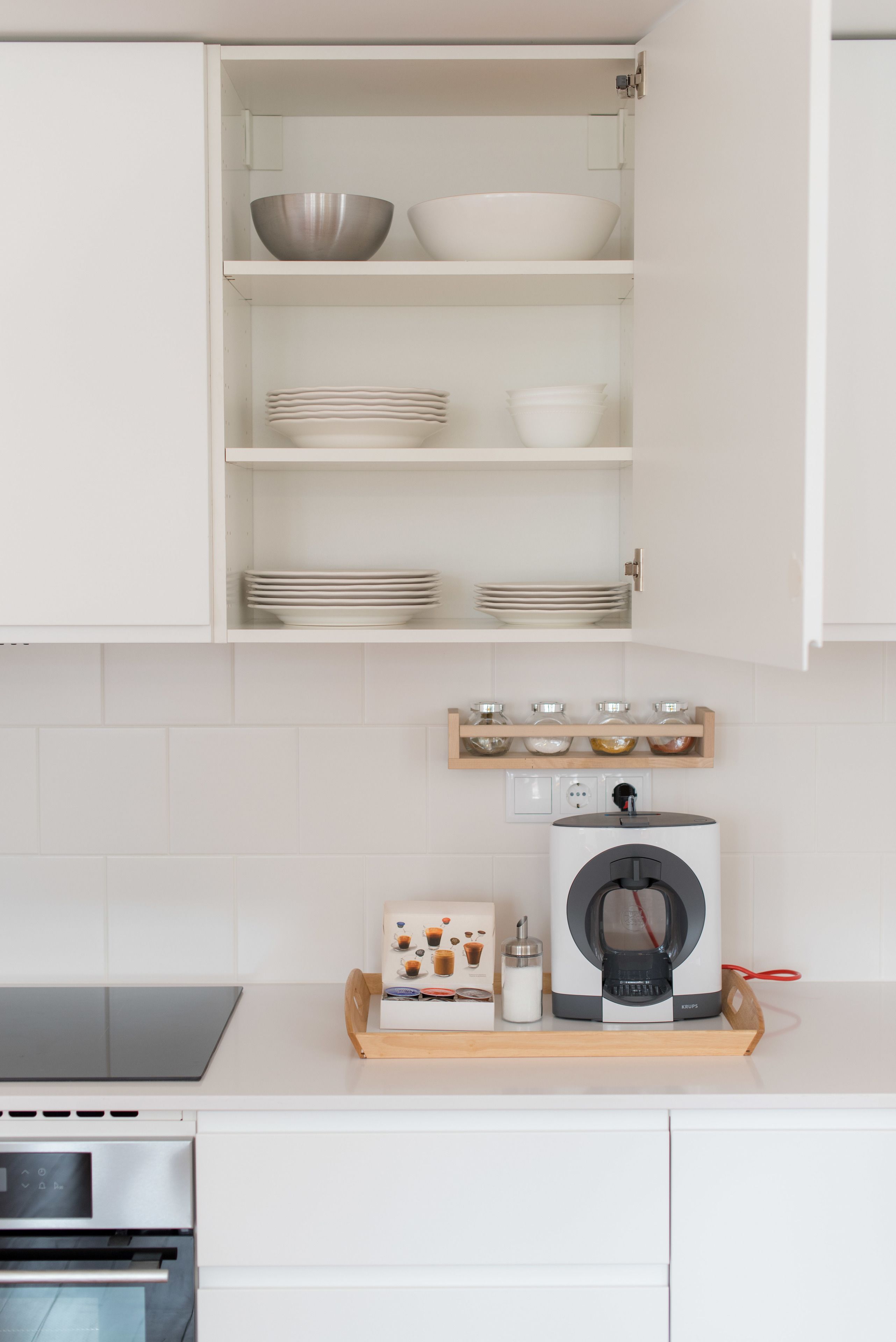 A kitchen with white cabinets, a built-in oven, and a coffee machine on a wooden tray.