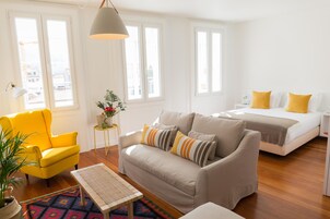 Ein heller, moderner Raum mit einer Couch, einem Sessel und einem Bett.