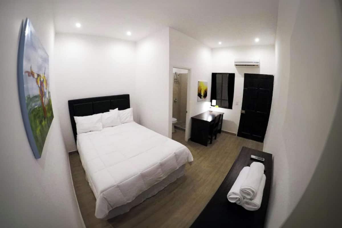 A hotel room with a bed, a desk, a mirror, and a bathroom.