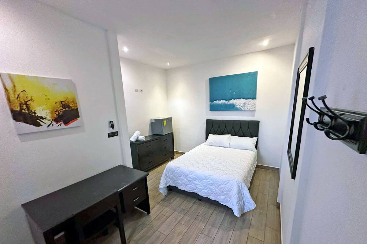 A hotel room with a bed, a desk, a dresser, and a painting on the wall.