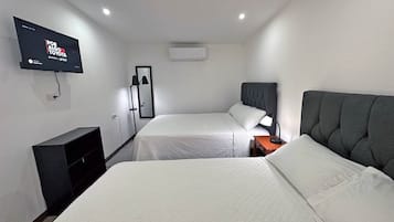 Habitación de hotel con dos camas, una televisión montada en la pared, un espejo y una mesita de noche con lámpara.