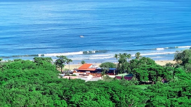 A coastal view with a beach, ocean, and buildings surrounded by greenery. - Surf Ranch Tamarindo (Tamarindo)