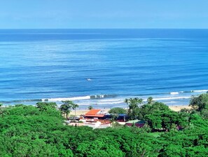 A coastal view with a beach, ocean, and buildings surrounded by greenery. - Surf Ranch Tamarindo (Tamarindo)