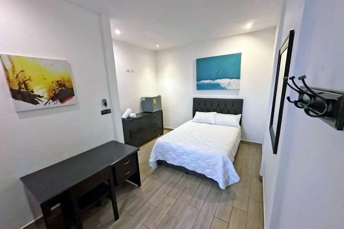 A bedroom with a bed, a desk, and two paintings on the walls.