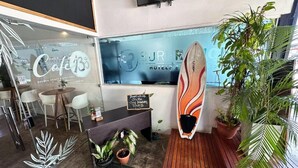 A modern cafe with a wooden floor, white chairs, a counter with a sign offering shuttle services, and a surfboard decoration. - Surf Ranch Tamarindo (Tamarindo)