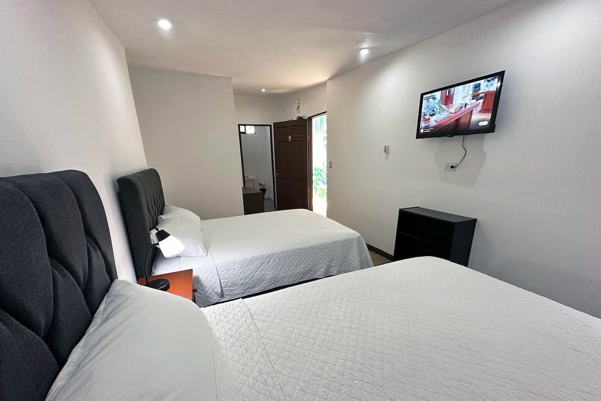 A hotel room with two beds, a TV on the wall, and a door leading to a bathroom.