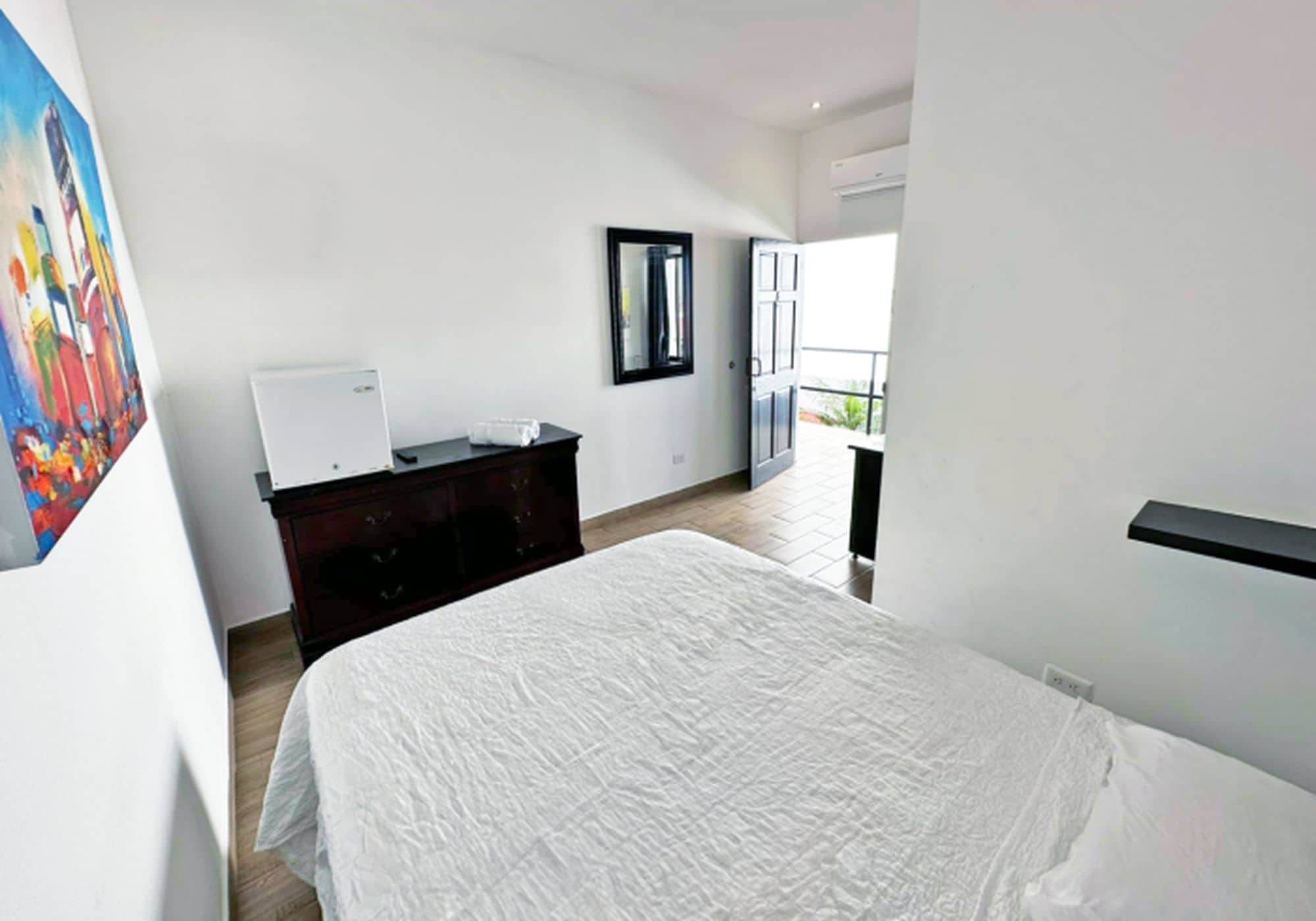 A hotel room with a bed, dresser, mirror, and a painting on the wall.