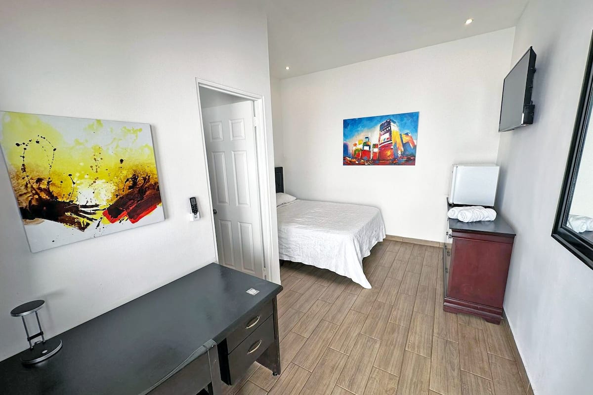 A hotel room with a bed, a desk, and two paintings on the walls.