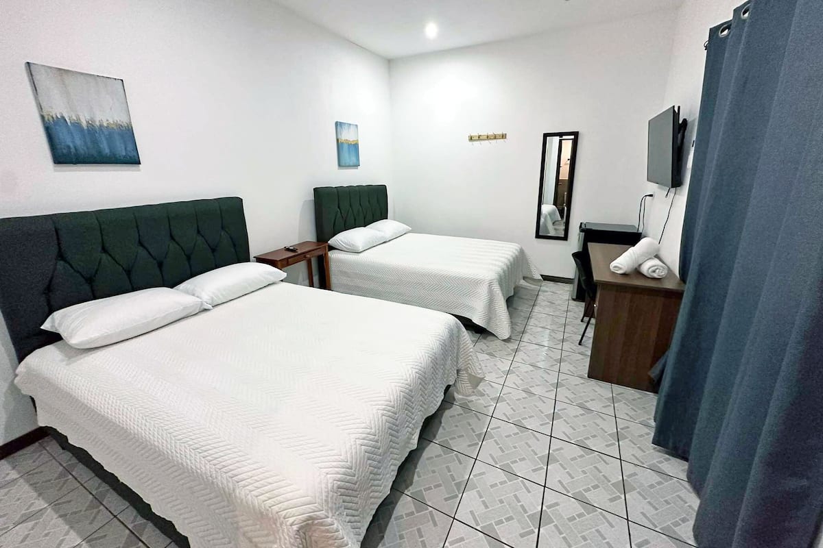 A hotel room with two beds, a desk, a mirror, and artwork on the walls.